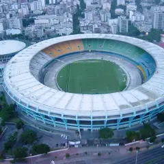 Widok z lotu ptaka na stadion Maracanã z zieloną murawą i kolorowymi trybunami, otoczony miejską zabudową.