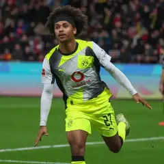 Piłkarz Adeyemi w żółto-szarej koszulce BVB z numerem 27, z afro na głowie, świętuje bramkę na boisku.