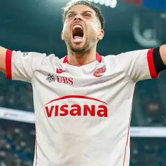 Piłkarz w białej koszulce z czerwonymi detalami, z rękami uniesionymi w geście triumfu, krzyczy z radości. To jego chwila, prawdziwy beniaminek na boisku!