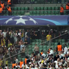 Tłum kibiców na trybunach, wśród nich stewardzi w kamizelkach i policja. Atmosfera napięcia, jakby pseudokibice mieli zaraz wywołać zamieszki.