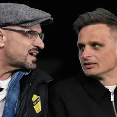 Dwóch mężczyzn rozmawia. Jeden w czapce i okularach, drugi z charakterystyczną fryzurą. Na kurtce jednego z nich widnieje napis "Wieczysta Kraków".