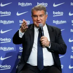 Prezes Barcelony, Joan Laporta, przemawia do mikrofonu na tle niebieskiej ścianki z logo klubu i sponsorów.
