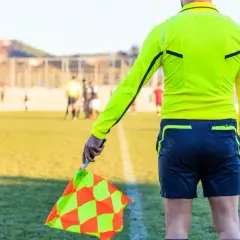 Sędzia liniowy z chorągiewką w ręku, gotowy do oceny akcji na boisku. Każdy mecz to szansa na zdobycie punktów do rankingu UEFA.