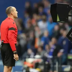 Sędzia w czerwonej koszulce czeka na decyzję VAR, która może skutkować żółtą kartką.