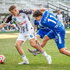 Piłkarze walczą o piłkę na boisku. Jeden w białej koszulce, drugi w niebieskiej z numerem 11. To ważny mecz, który może wpłynąć na 3. liga tabelę.