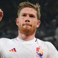 Kevin De Bruyne w białej koszulce z godłem Belgii, unosi palec wskazujący w geście triumfu.
