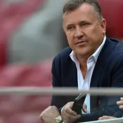Prezes PZPN w garniturze, z telefonem w dłoni, siedzi na trybunach stadionu.