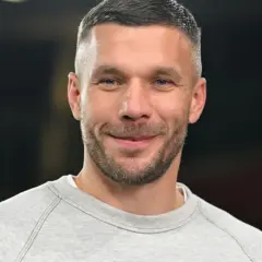 Uśmiechnięty Łukasz Podolski w szarej bluzie. Jego kariera piłkarska i biznesy budują imponujący lukas podolski majątek.