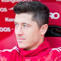 Robert Lewandowski siedzi na czerwonej ławce w czerwonej bluzie z białymi paskami.