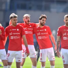 Piłkarze Wisły Kraków w czerwonych strojach, dyskutują o potencjalnych transferach.