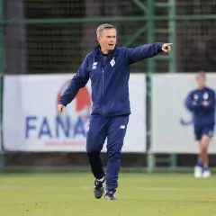Trener klubu piłkarskiego z Kijowa w niebieskim dresie wskazuje kierunek na boisku.
