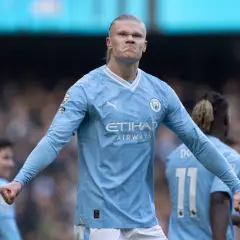 Erling Haaland, najdroższy piłkarz świata, w błękitnej koszulce Manchesteru City, z zaciętą miną i zaciśniętą pięścią.