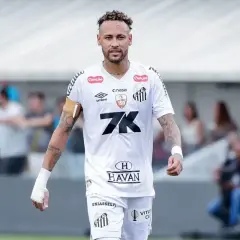 Neymar w białej koszulce Santos, z opaską na ramieniu, na boisku. To właśnie tam gra Neymar, kiedyś gwiazda tego klubu.