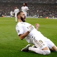 Karim Benzema świętuje zwycięstwo w Lidze Mistrzów, klęcząc na boisku w białej koszulce Realu Madryt.