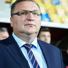 Selekcjoner w okularach, w garniturze i krawacie, z uwagą obserwuje wydarzenia na boisku.