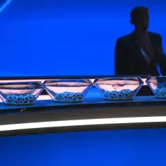 Cztery szklane misy z piłkami Ligi Mistrzów czekają na losowanie. W tle sylwetka mężczyzny.