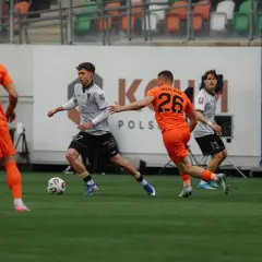 Piłkarze Cracovii i Pogoni Szczecin walczą o piłkę na boisku. Dąbrowski (8) w pomarańczowej koszulce i Kolan (26) w tej samej barwie.