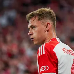 Joshua Kimmich, spocony po meczu, w białej koszulce z czerwonymi pasami i logo Audi.