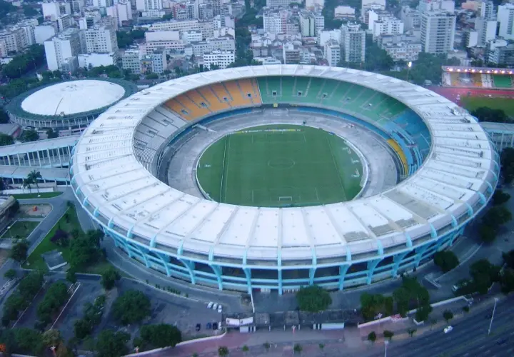 Widok z lotu ptaka na stadion Maracanã z zieloną murawą i kolorowymi trybunami, otoczony miejską zabudową.