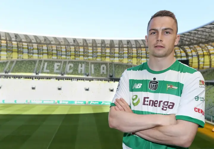 Piłkarz Lechii Gdańsk, gajos w zielono-białej koszulce, stoi na tle stadionu.
