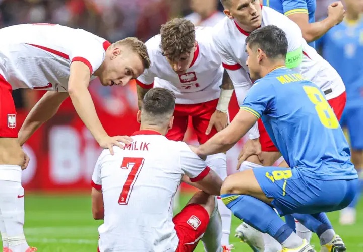 Piłkarze otaczają kolegę z drużyny, który doznał kontuzji. Widoczna jest koszulka z napisem "MILIK" i numerem 7.