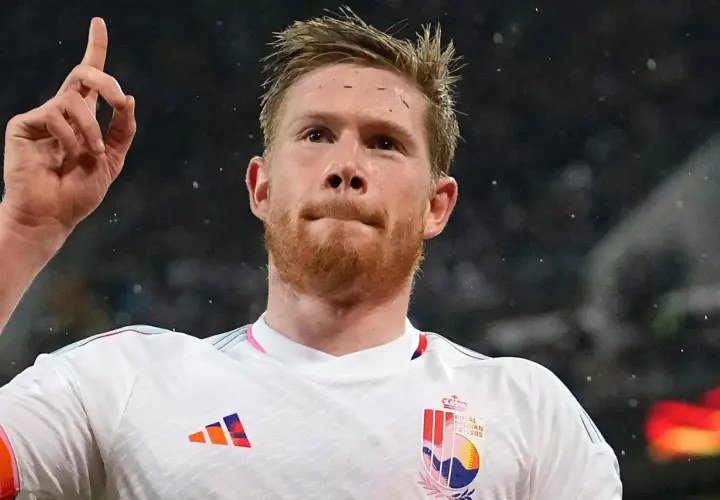 Kevin De Bruyne w białej koszulce z godłem Belgii, unosi palec wskazujący w geście triumfu.