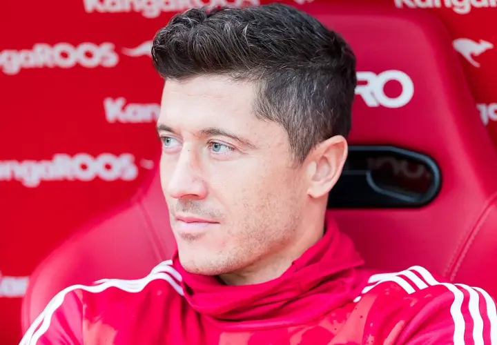 Robert Lewandowski siedzi na czerwonej ławce w czerwonej bluzie z białymi paskami.