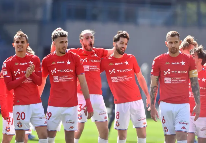 Piłkarze Wisły Kraków w czerwonych strojach, dyskutują o potencjalnych transferach.