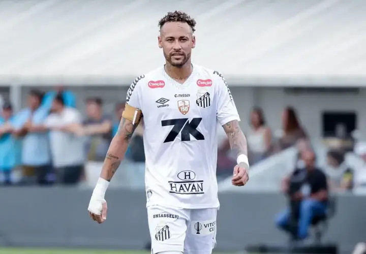 Neymar w białej koszulce Santos, z opaską na ramieniu, na boisku. To właśnie tam gra Neymar, kiedyś gwiazda tego klubu.