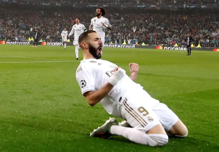 Karim Benzema świętuje zwycięstwo w Lidze Mistrzów, klęcząc na boisku w białej koszulce Realu Madryt.