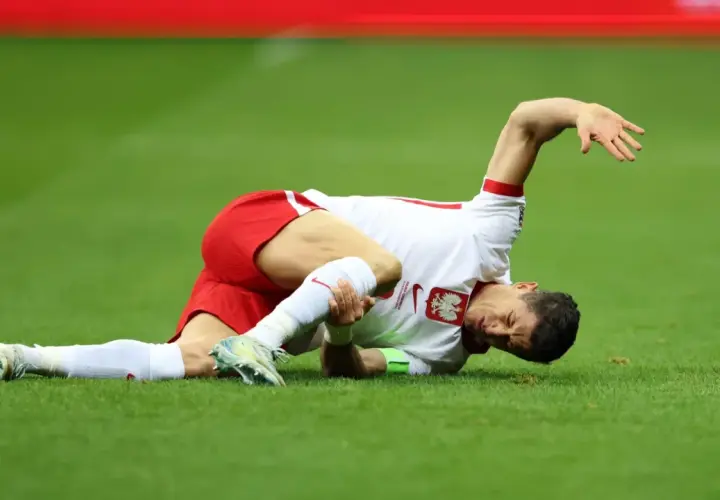 Robert Lewandowski leży na trawie, trzymając się za nogę. Wygląda na to, że to poważna lewandowski kontuzja.