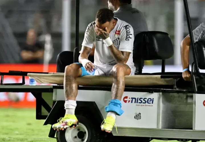 Neymar siedzi na wózku golfowym, zakrywając twarz dłońmi. Jego kontuzja jest widoczna na nogach.