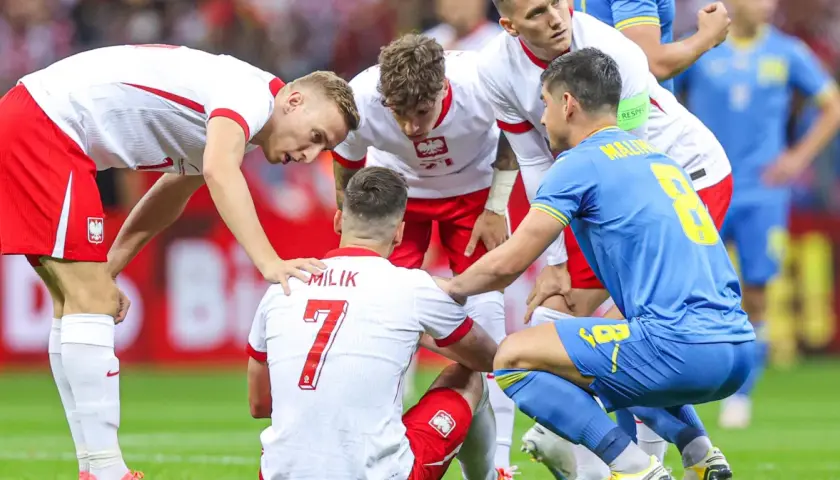 Piłkarze otaczają kolegę z drużyny, który doznał kontuzji. Widoczna jest koszulka z napisem "MILIK" i numerem 7.