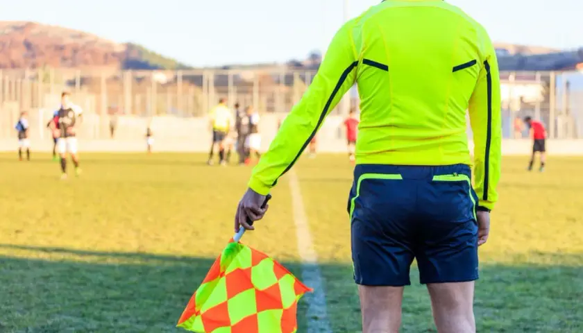 Sędzia liniowy z chorągiewką w ręku, gotowy do oceny akcji na boisku. Każdy mecz to szansa na zdobycie punktów do rankingu UEFA.