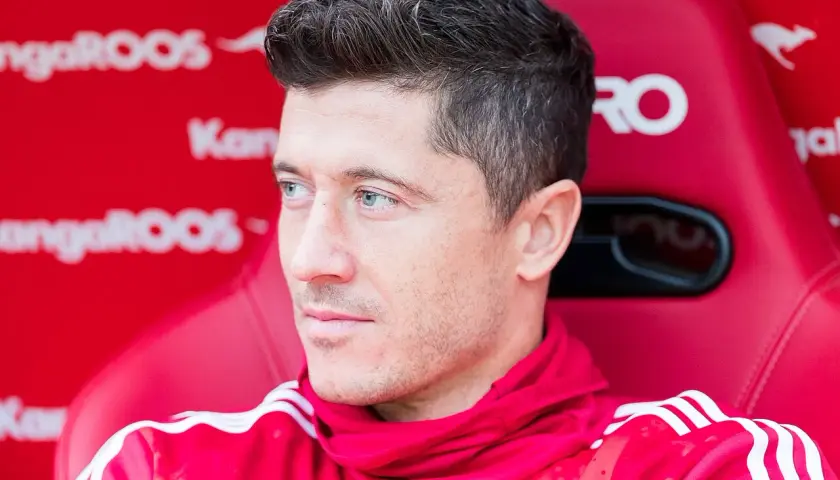 Robert Lewandowski siedzi na czerwonej ławce w czerwonej bluzie z białymi paskami.