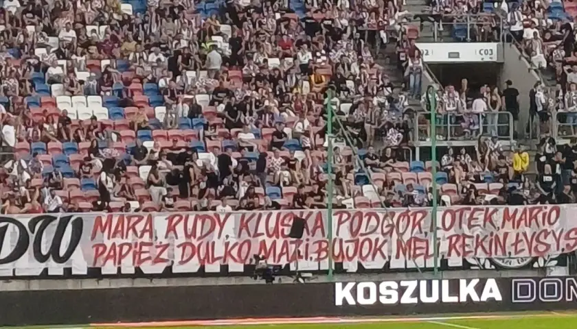 Tłum kibiców na trybunach, transparent z nazwiskami piłkarzy i hasłem "torcida".