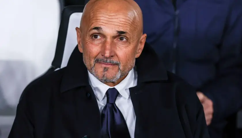 Łysy mężczyzna z brodą, ubrany w białą koszulę i granatowy krawat, w ciemnym płaszczu. To trener Juventusu, wpatrzony w dal.