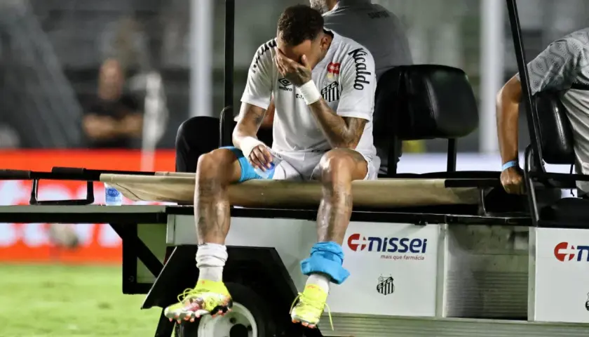 Neymar siedzi na wózku golfowym, zakrywając twarz dłońmi. Jego kontuzja jest widoczna na nogach.