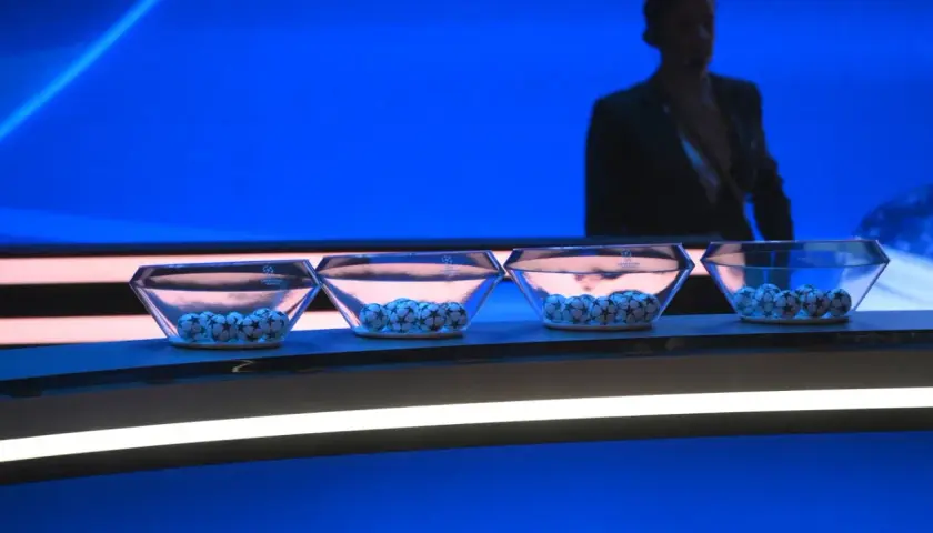 Cztery szklane misy z piłkami Ligi Mistrzów czekają na losowanie. W tle sylwetka mężczyzny.