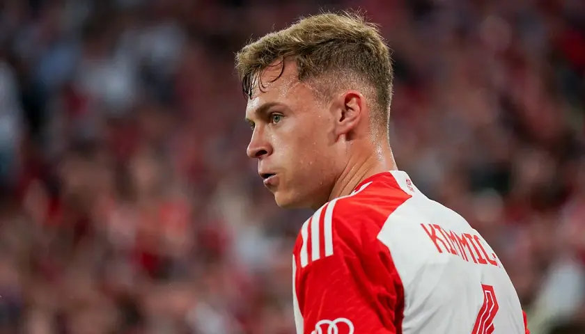 Joshua Kimmich, spocony po meczu, w białej koszulce z czerwonymi pasami i logo Audi.