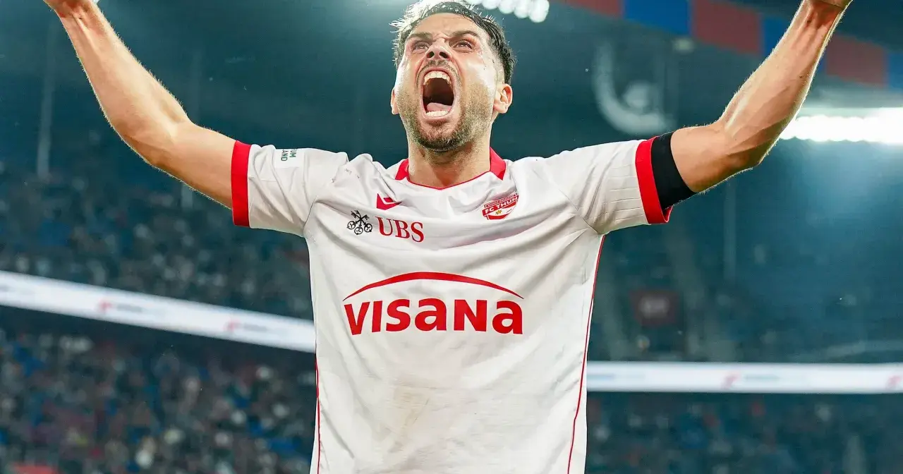 Piłkarz w białej koszulce z czerwonymi detalami, z rękami uniesionymi w geście triumfu, krzyczy z radości. To jego chwila, prawdziwy beniaminek na boisku!