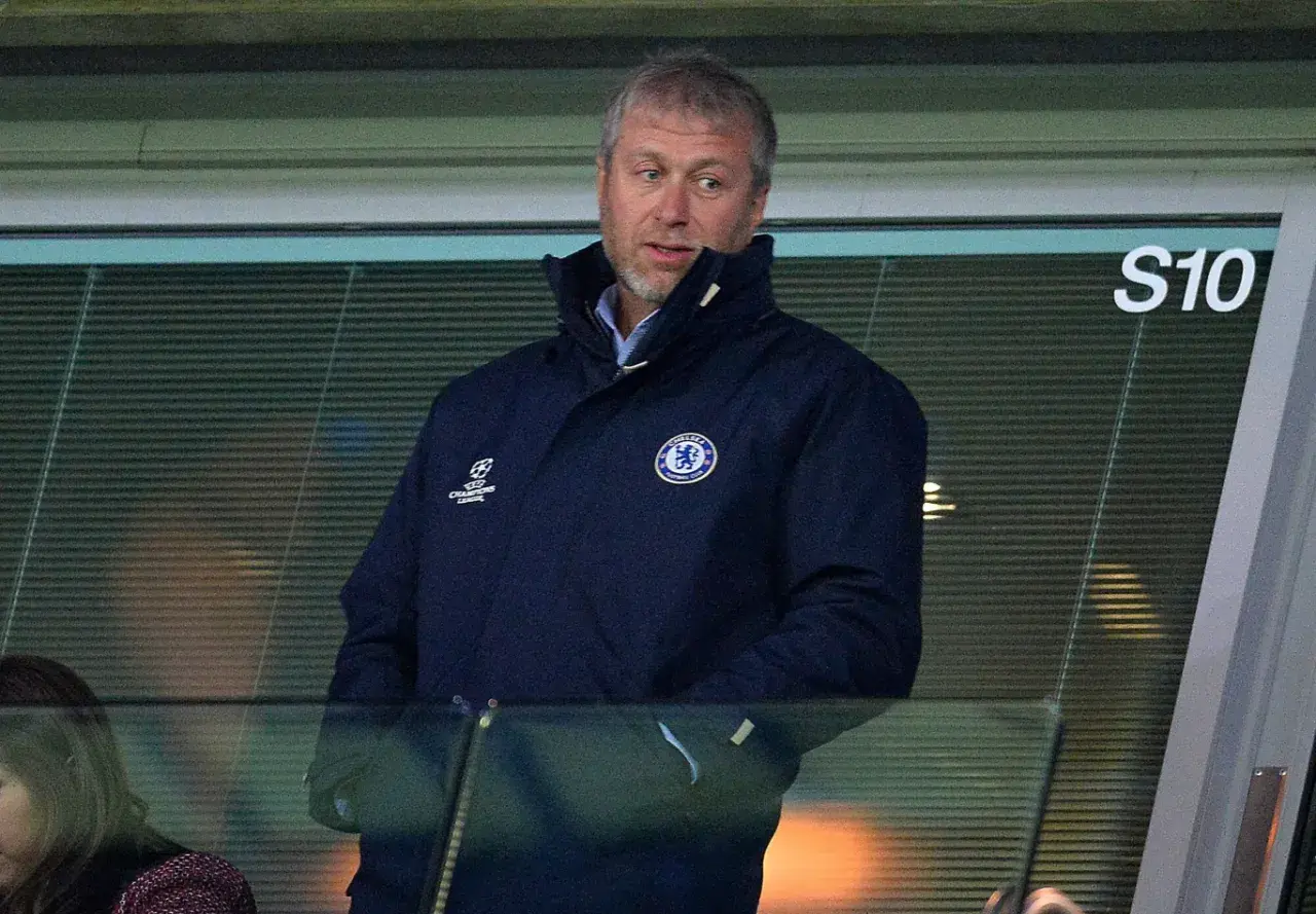 Roman Abramowicz w kurtce Chelsea FC, z emblematem Ligi Mistrzów, ogląda mecz z trybun.