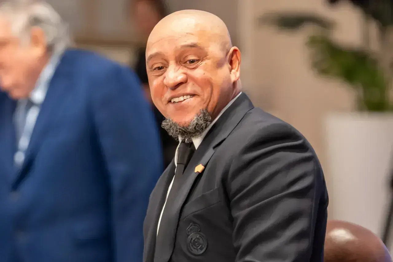 Uśmiechnięty Roberto Carlos w garniturze, z charakterystyczną brodą. Widać herb Realu Madryt. Roberto Carlos żyje i ma się dobrze!