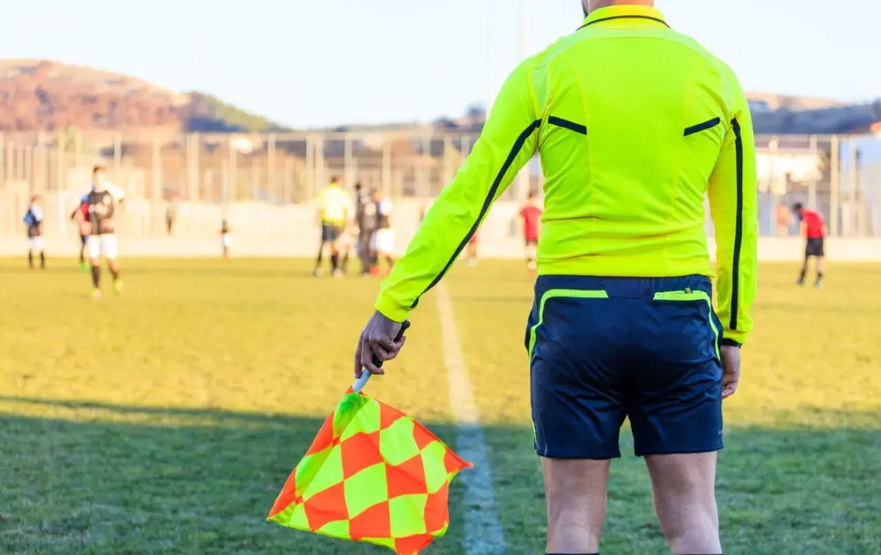 Sędzia liniowy z chorągiewką w ręku, gotowy do oceny akcji na boisku. Każdy mecz to szansa na zdobycie punktów do rankingu UEFA.