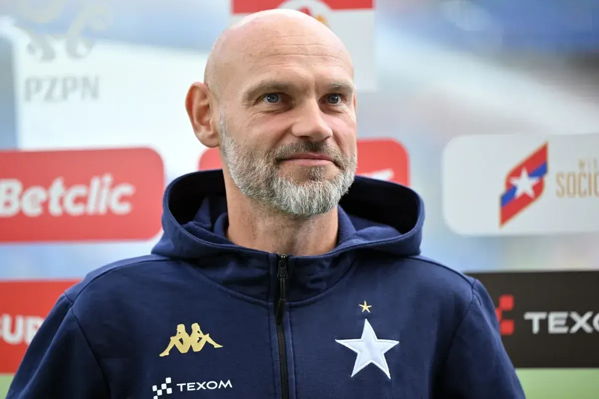 Łysy mężczyzna z siwą brodą, trener Wisły Kraków, w granatowej bluzie z kapturem z logo klubu.