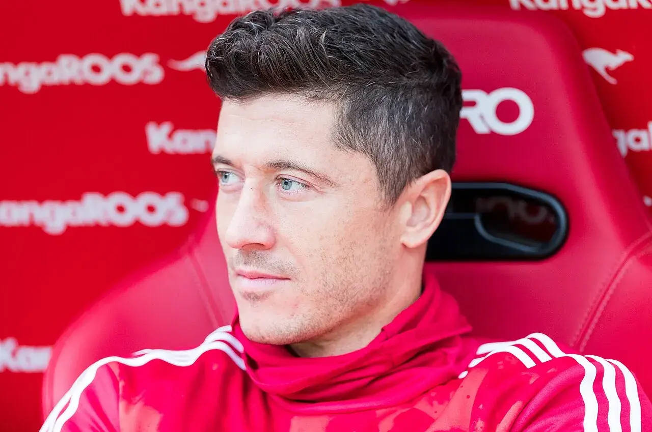 Robert Lewandowski siedzi na czerwonej ławce w czerwonej bluzie z białymi paskami.