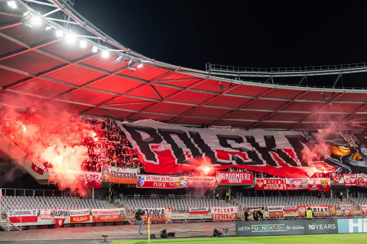 Tłum ultrasi na stadionie, odpalone race i ogromny transparent "POLSKA".