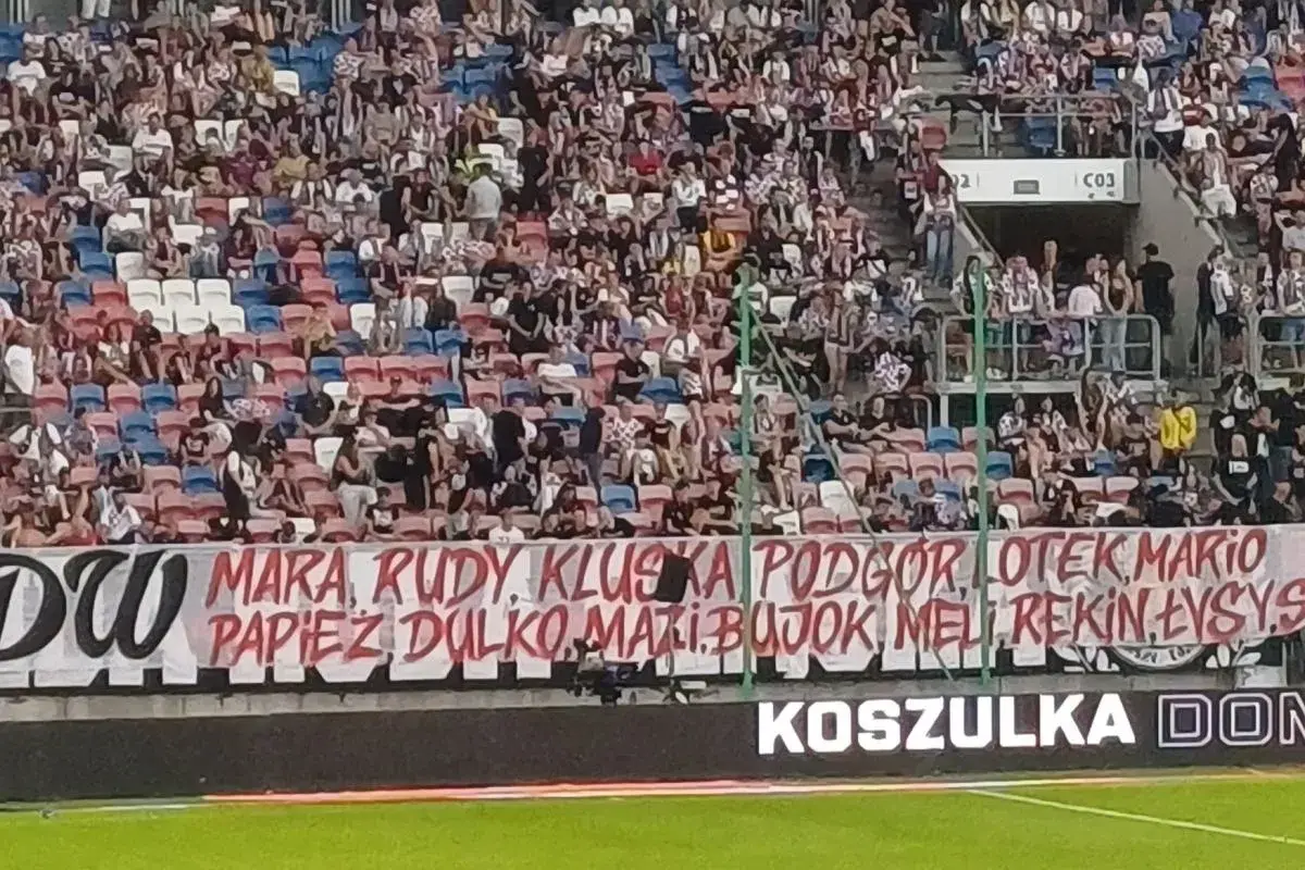 Tłum kibiców na trybunach, transparent z nazwiskami piłkarzy i hasłem "torcida".