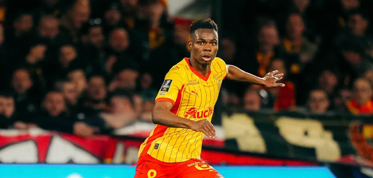 Piłkarz RC Lens w żółto-czerwonej koszulce biegnie po boisku, gotowy do akcji przeciwko Stade Rennais.