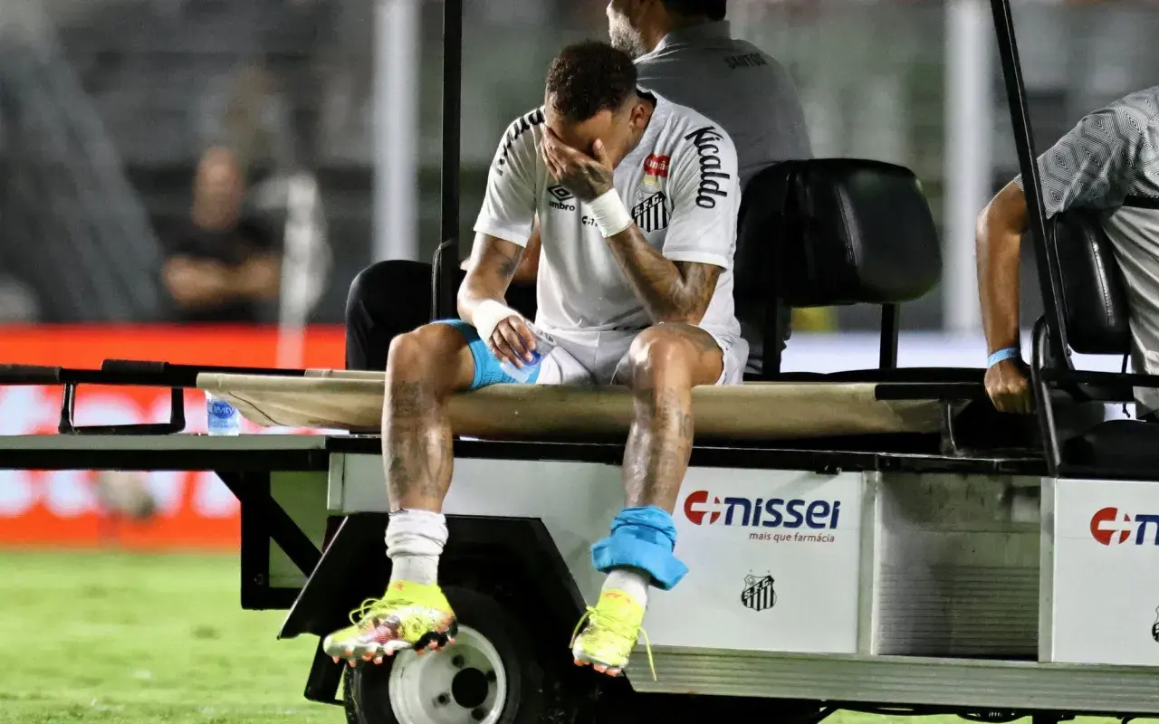 Neymar siedzi na wózku golfowym, zakrywając twarz dłońmi. Jego kontuzja jest widoczna na nogach.